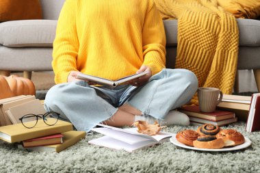 Evde halıda çöreklerle kitap okuyan bir kadın.