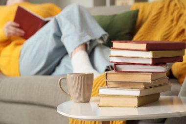 Masada kahve fincanı olan kitap yığını. Evde kitap okuyan bir kadına karşı. Yakın çekim.