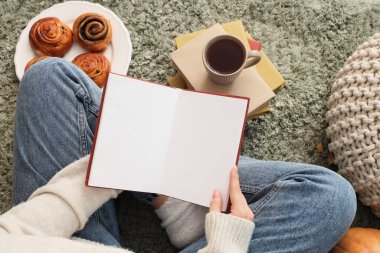 Boş kitabı olan bir kadın, kahve fincanı ve çörekleri halıya oturmuş, üst tarafta.