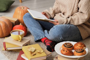Evde çay fincanı ve halıda çöreklerle kitap okuyan bir kadın.