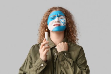 Yüzünde İsrail 'in boyalı bayrağı ve ışık arka planında yanan mumla dua eden genç bir kadın. Uluslararası Soykırım Anma Günü