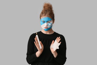 Yüzü boyalı genç bir kadın yanan bir mum ve arka planda Yahudi rozeti tutuyor. Uluslararası Soykırım Anma Günü