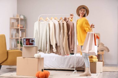 Sonbahar günü yatak odasında alışveriş çantaları ve elbise askısı olan genç bir kadın.