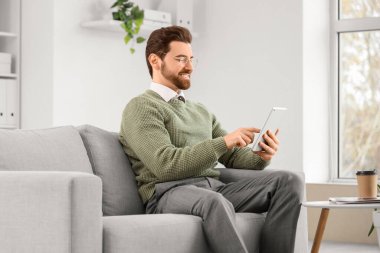 Ofisteki kanepede tablet bilgisayarla çalışan yakışıklı adam.