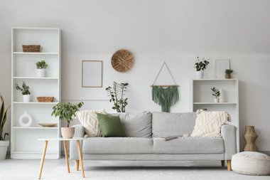 Gri kanepe, raf üniteleri ve bitkilerle aydınlık oturma odasının içinde.