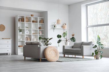 Gri kanepeleri, raf ünitesi ve bitkileriyle aydınlık oturma odasının içinde.