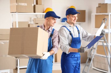 Depoda kutu ve pano taşıyan erkek yükleyiciler