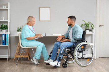 Hastanede tekerlekli sandalyede genç bir adamla çalışan kadın doktor.