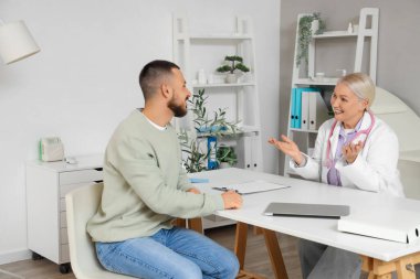 Klinikteki masada genç bir adamla çalışan kadın doktor.