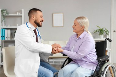 Hastanede tekerlekli sandalyede el ele tutuşan olgun bir kadınla erkek doktor.