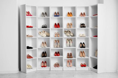 Farklı kadın ayakkabıları olan raf ünitesi odada ışık duvarının yanında.