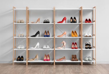Farklı kadın ayakkabıları olan raf ünitesi odada ışık duvarının yanında.