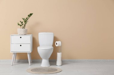 Tuvaletin içinde klozet, komodin ve bej duvarın yanında bitkiler var.