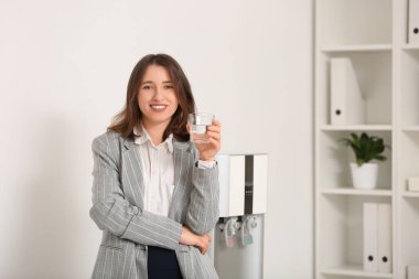 Ofisteki soğutucudan su içen gülümseyen genç kadın.