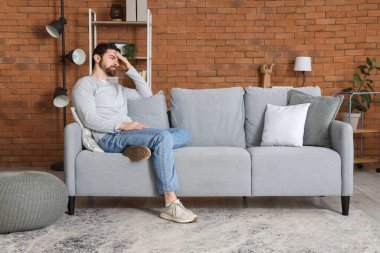 Evdeki kanepede oturan endişeli adam.