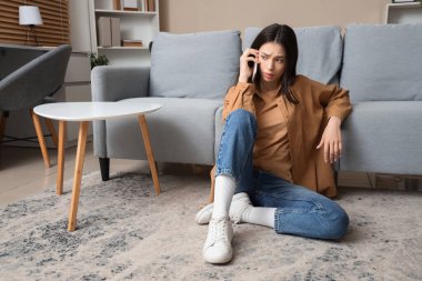 Evde cep telefonuyla konuşan endişeli genç bir kadının portresi