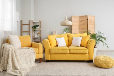 Şık bir oturma odası, rahat sarı koltuk, kanepe ve puf.