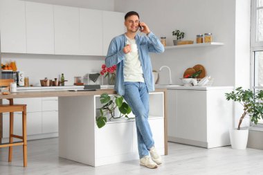 Elinde çay fincanı olan yakışıklı genç adam mutfakta telefonla konuşuyor.