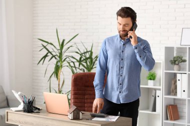 Ofiste cep telefonuyla konuşan, hesap makineli genç bir işadamı.