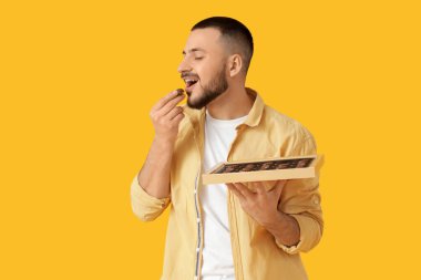 Sarı arka planda çikolata yiyen genç adam.