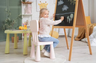 Yatak odasındaki tahtaya resim çizen şirin küçük kız.