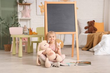 Oyuncak ve tebeşirle evde yerde oturan tatlı küçük kız.