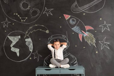 Siyah duvarın yanındaki masada oturan şirin küçük çocuk.