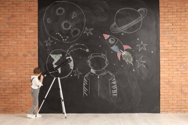 Teleskopla siyah duvarın yakınına bakan sevimli küçük çocuk.