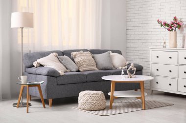 Rahat kanepe, koltuk ve sandık dolusu çekmece. Oturma odasının içinde çiçek açan manolya dalları var.