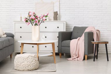 Oturma odasının içinde çiçek açan manolya dalları olan kanepe, koltuk ve kahve masası.