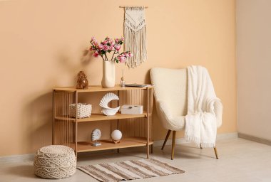 Oturma odasındaki şık koltuğun yanındaki konsol masasında çiçek açan vazo.