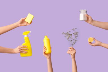 Birçok kadın eli mor arka planda deterjan, sünger ve çiçeklerle dolu.