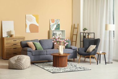 Kanepe, koltuk ve çiçek açan manolya dalları oturma odasının içindeki sehpanın üzerindeki vazoda.