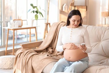 Evde koltukta oturan glukometresi olan hamile bir kadın. Gebelik Diyabet Konsepti