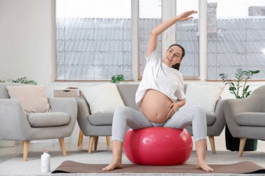 Genç hamile kadın evde fitbol antrenmanı yapıyor.