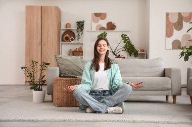 Mutlu genç kadın oturma odasında yerde meditasyon yapıyor.