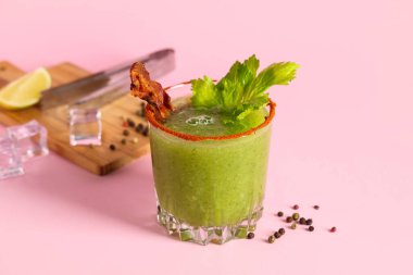Pembe arka planda pastırma ve kereviz ile süslenmiş bir bardak Bloody Mary kokteyli.