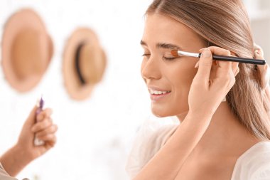 Profesyonel makyöz stüdyoda genç bir kadına göz farı uyguluyor.