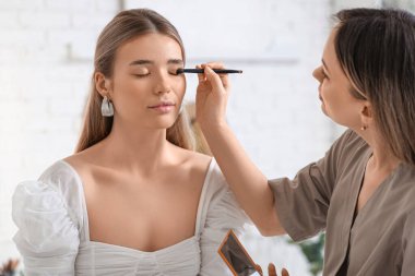 Profesyonel makyöz stüdyodaki genç bayana göz farı uyguluyor.