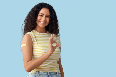 Mavi arka plandaki aşıdan sonra sağlık bandı olan genç Afro-Amerikalı kadın iyi görünüyor.