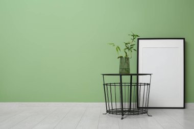 Kahve masasında bambu saplı vazo ve yeşil duvarın yanında boş çerçeve.