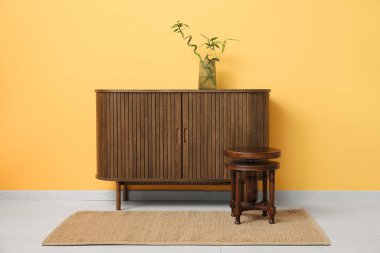 Turuncu duvarın yanındaki ahşap dolapta bambu dalları olan vazo.