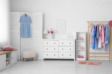 Açık renk soyunma odasının içinde askılık, çekmeceler ve katlanır ekran var.