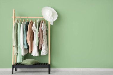 Elbise askısı, şık kıyafetler ve yeşil duvarın yanında şapka.