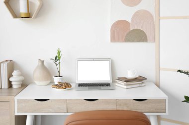 Ev ofisinde boş dizüstü bilgisayar, kurabiye ve kahve fincanı olan bir işyeri.