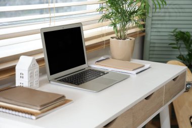 Oda penceresinin yanında dizüstü bilgisayarı olan rahat bir iş yeri.