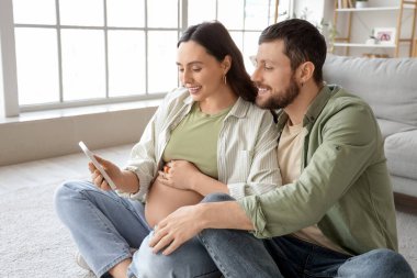 Mutlu hamile çift evde cep telefonu kullanıyor.