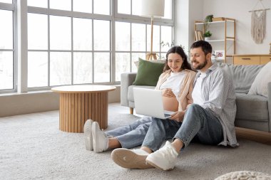 Evde dizüstü bilgisayar kullanan mutlu hamile çift.