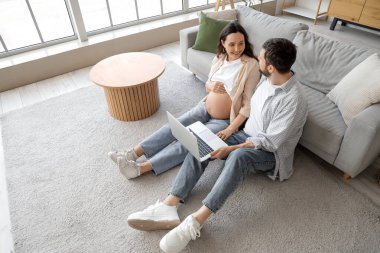 Evde dizüstü bilgisayar kullanan mutlu hamile çift.