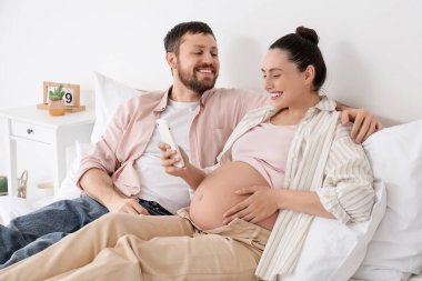 Mutlu hamile çift yatak odasında cep telefonu kullanıyor.